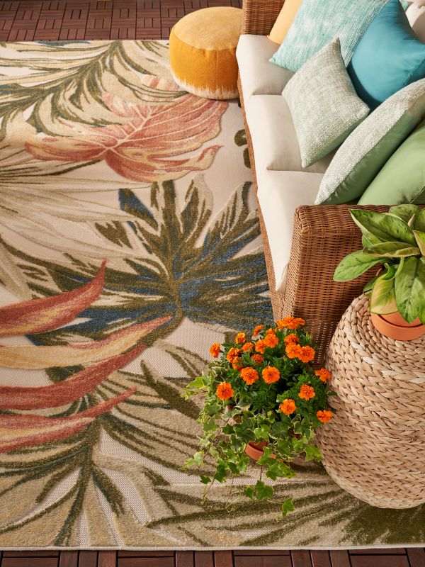 Angled overhead view of a colorful tropical rug under a sofa decorated with outdoor pillows