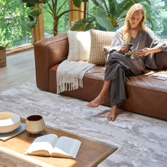 Woman seated in a living room with textured pillows, plants, and an abstract rug
