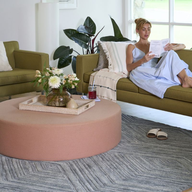 Woman seated in a living room with a textured blue rug, blankets, and pillows