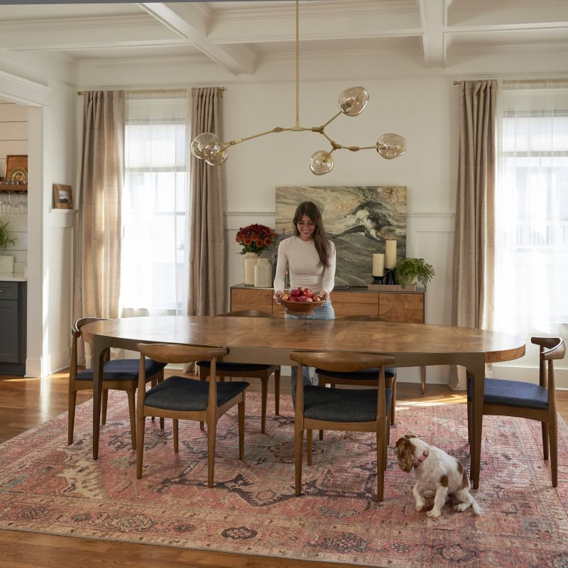 Woman setting a bowl of apples on a dining room table with vintage-style rug