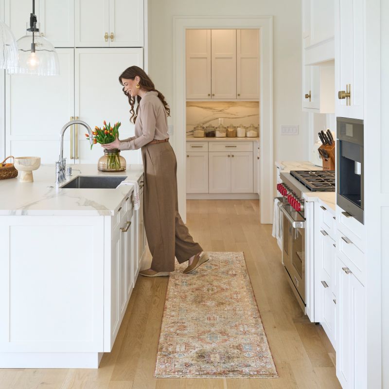 Woman in a kitchen placing flowers in a planter with vintage-style runner