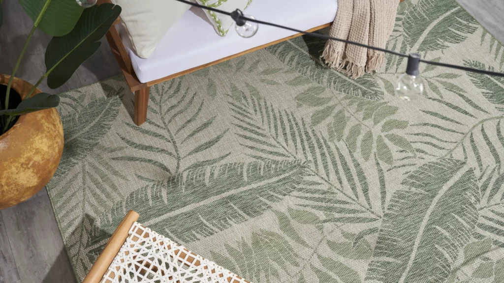 Nourison Garden Oasis GOA02 ivory green palm leaf outdoor rug on a grey wood deck with teak furniture and string lights overhead