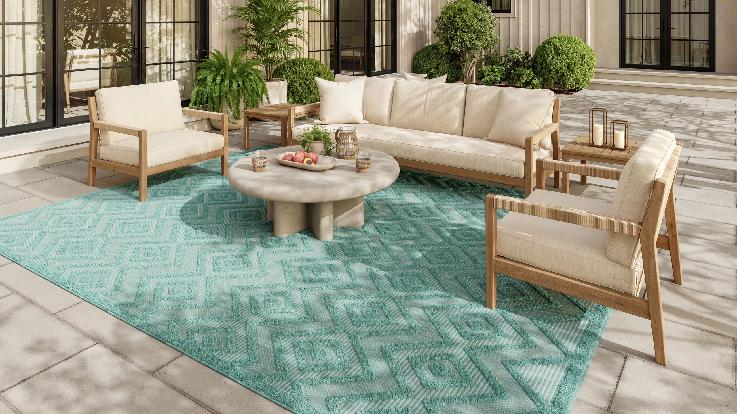 Aqua teal Nourison NRV01 outdoor rug styled on a stone patio with teak furniture and lush greenery