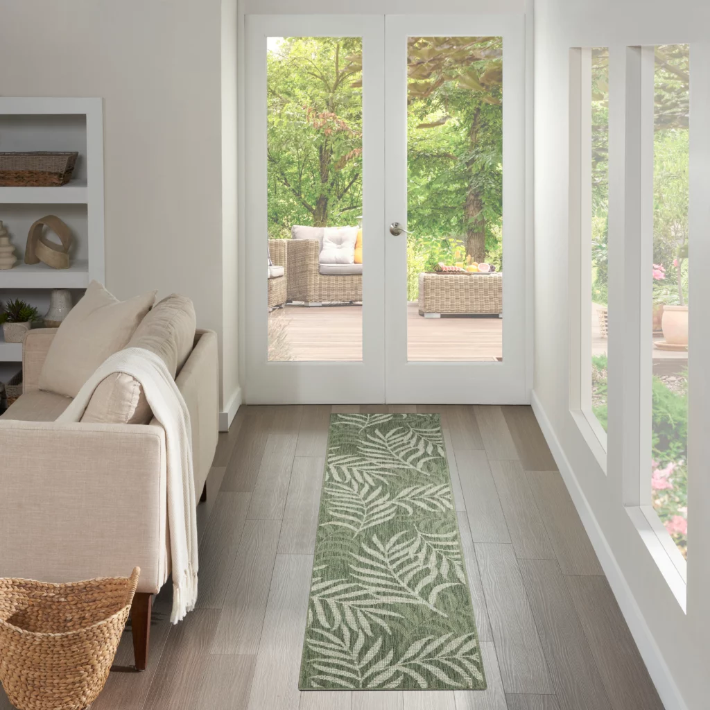 Green and ivory botanical runner rug laid on a hardwood floor inside a bright living space with French doors opening to an outdoor deck.
