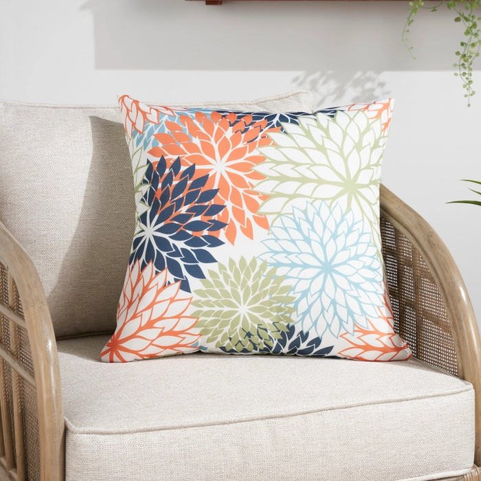 Aloha ALH05 multicolor throw pillow with bold floral burst pattern in orange, navy, sage, and blue on a wicker outdoor chair