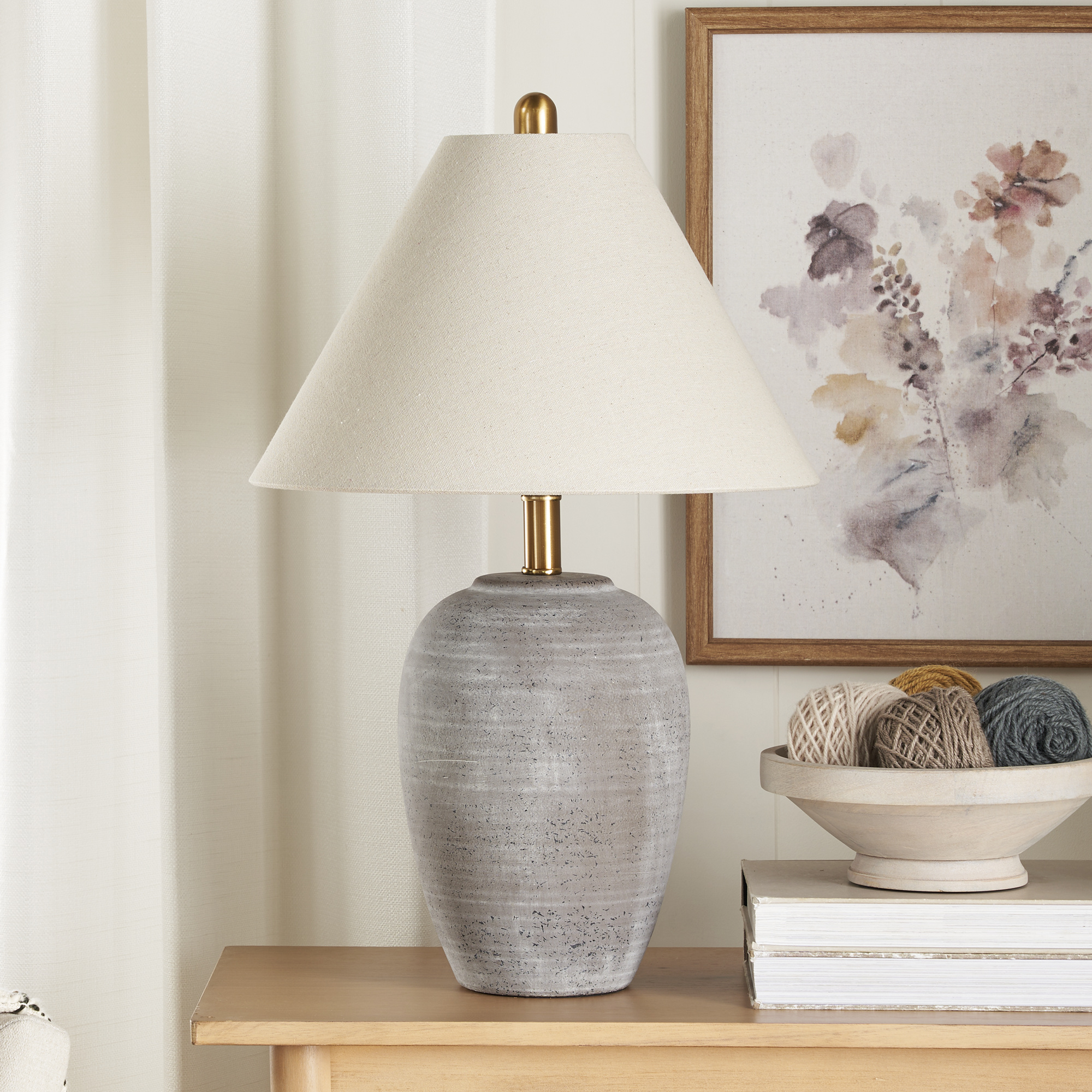 Rustic gray ceramic table lamp with a beige linen shade and brass hardware on a light wood console table