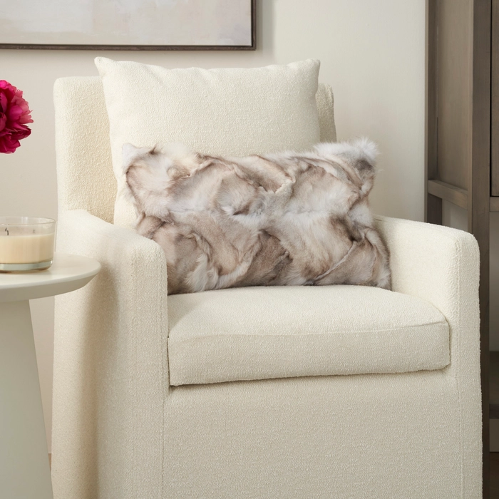 Mina Victory Couture Fur F7105 silver fox fur lumbar throw pillow on a cream bouclé armchair beside a white side table and candle