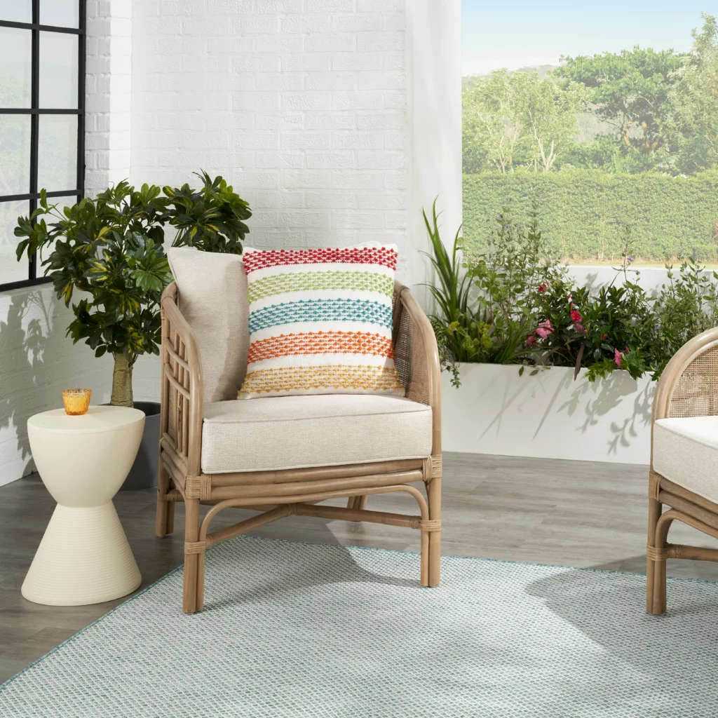 Mina Victory multicolor 18 by 18 outdoor pillow on a rattan lounge chair with a Nourison Aloha style rug visible in the foreground