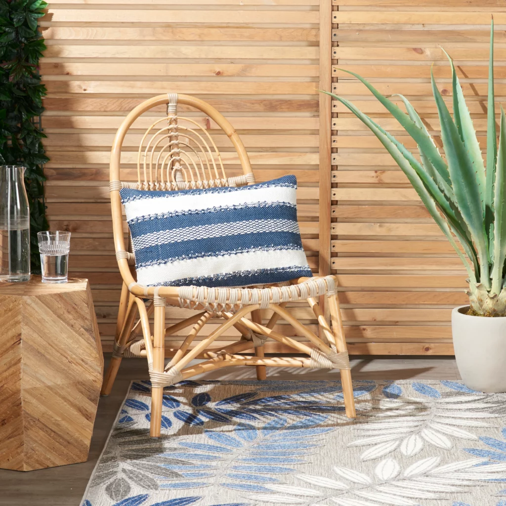 Mina Victory navy striped 14 by 20 lumbar outdoor pillow on a rattan chair in a patio setting with a patterned outdoor rug in the background