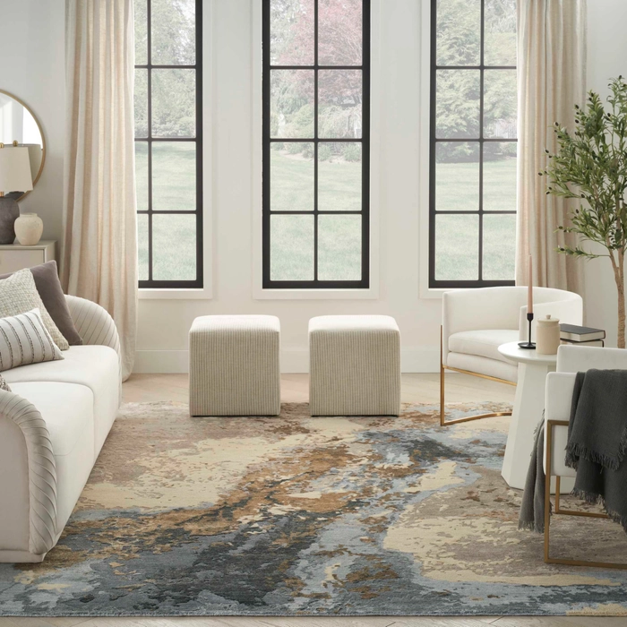Silk Shadows SHA23 beige blue abstract area rug in a bright modern living room with cream sofa, striped ottomans, and tall black-framed windows