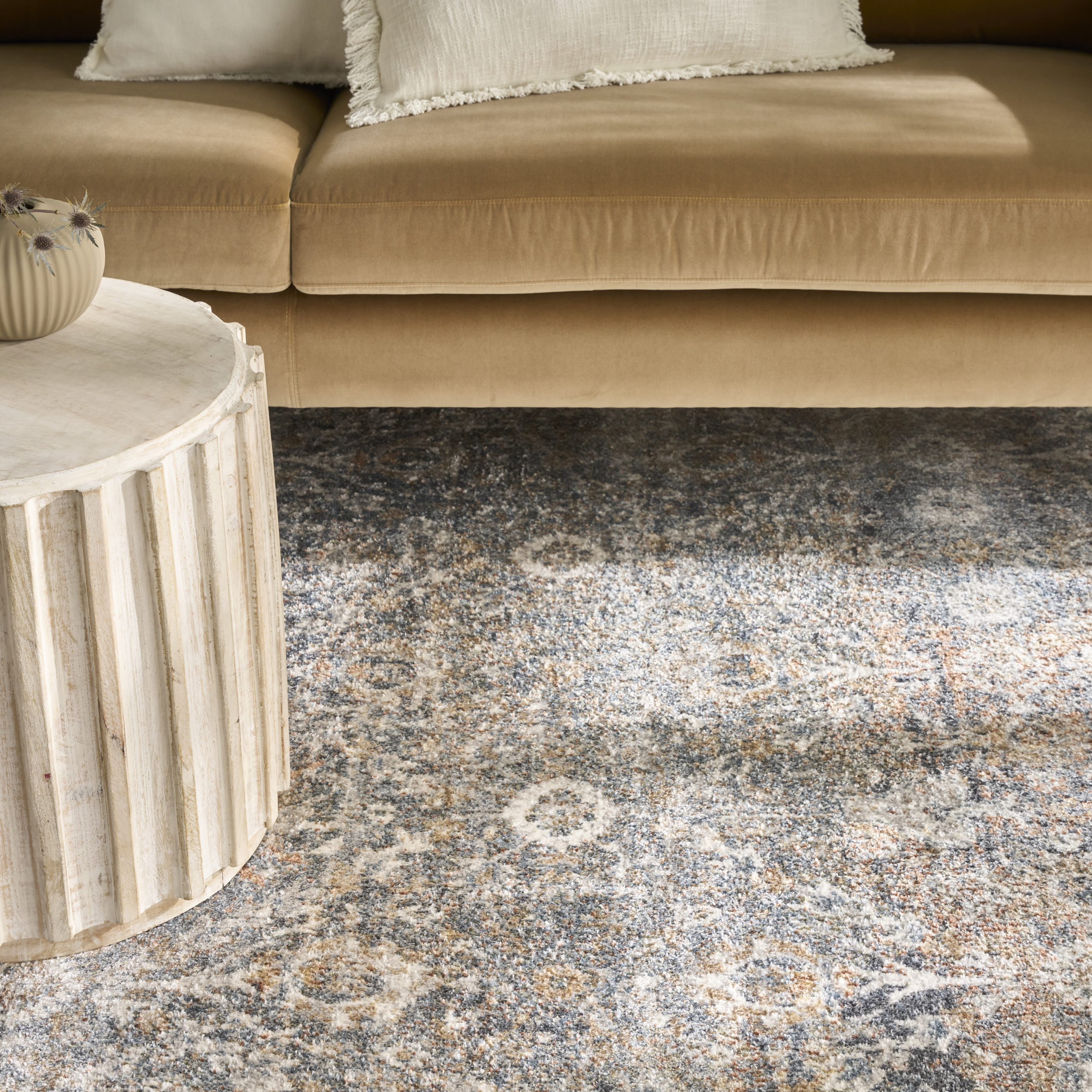 Vintage-style area rug in ivory, blue, and warm brown tones shown beneath a camel-colored sofa and stone coffee table
