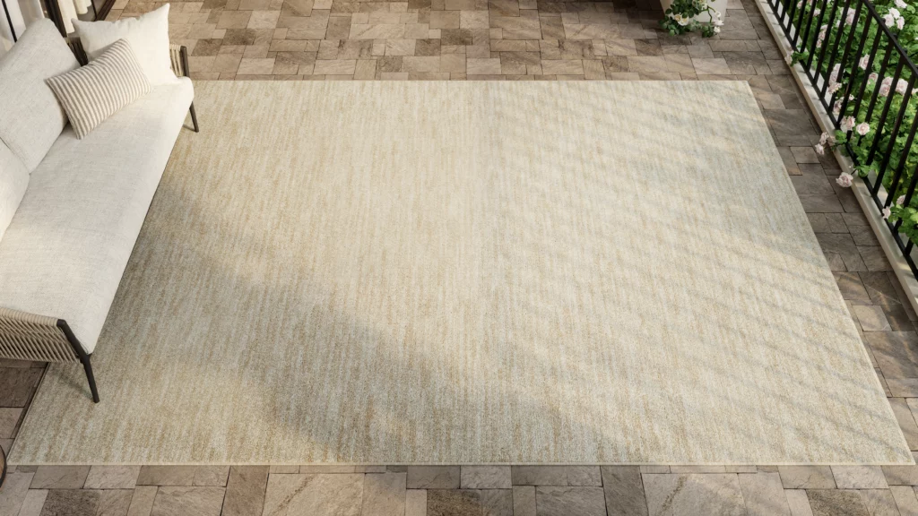 Nourison Essentials NRE01 ivory beige outdoor rug viewed from above on a stone balcony with a neutral outdoor sofa and wrought iron railing