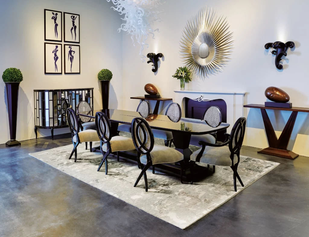 Silver and ivory abstract wool area rug beneath a black lacquer dining table with six ornate velvet chairs in a dramatic designer showroom with a sunburst mirror and glass chandelier