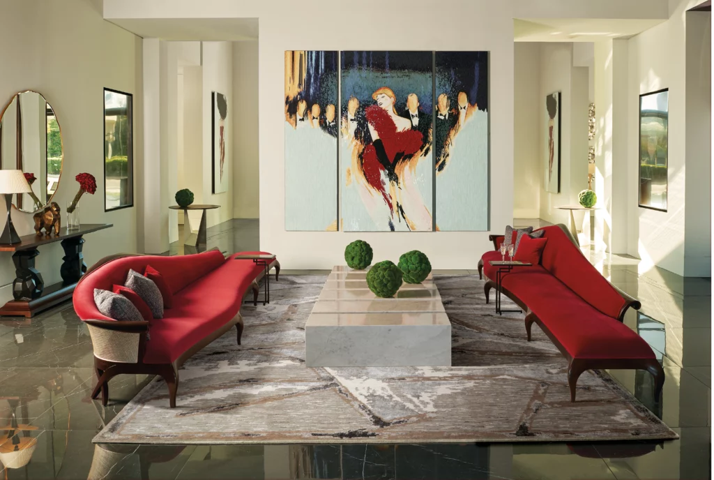 Silver grey abstract wool area rug anchoring a formal sitting room with two curved red sofas and a marble coffee table beneath a large figurative triptych painting