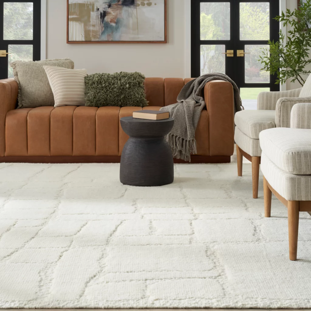 Ivory wool area rug with geometric trellis pattern in a neutral living room with a tan leather sofa and linen chairs