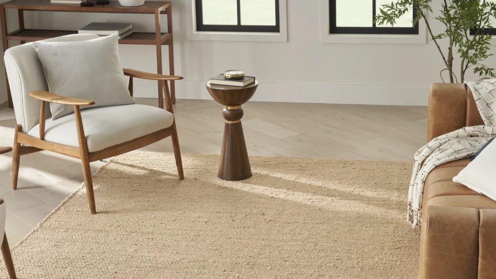 Bleached natural jute area rug styled in a bright living room with a mid-century accent chair, cognac leather sofa, and light hardwood floors
