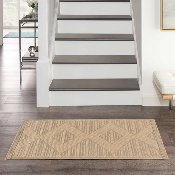 Natural beige geometric patterned accent rug placed at the base of a staircase with dark hardwood floors, grey wood stair treads, and white painted risers in a transitional entryway