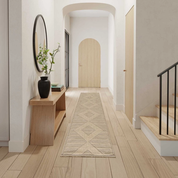 Natural beige geometric patterned runner rug styled in a bright modern hallway with light hardwood floors, a round black mirror, oak console table, and an arched wood door at the end of the corridor