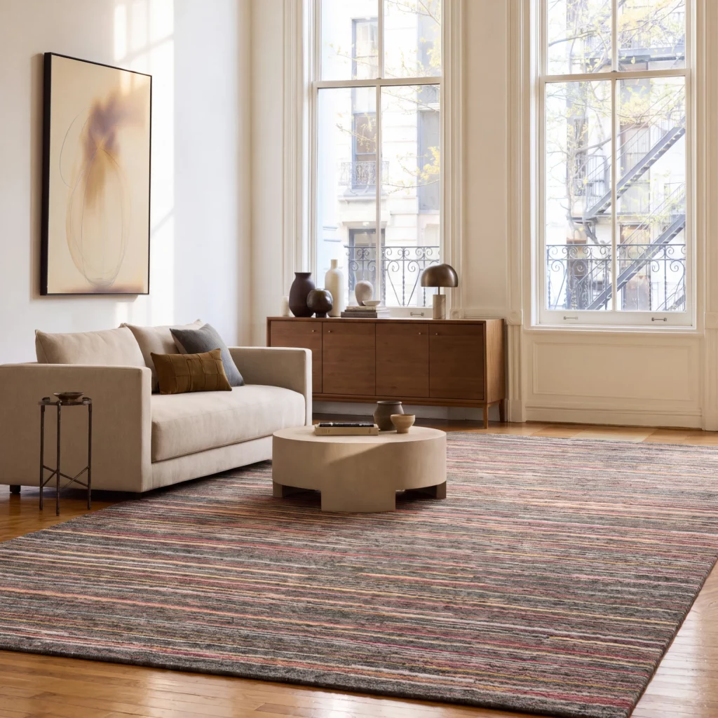 Plateau PAE01 Grey/Flame rug with red stripes on a soft grey ground, in a bright living room with a cream sofa and tall windows.