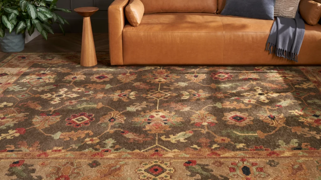 Close-up of the Nourison Tahoe TA10 Espresso wool area rug featuring a traditional floral pattern in rust, red, olive green, and gold beneath a tan leather sofa.